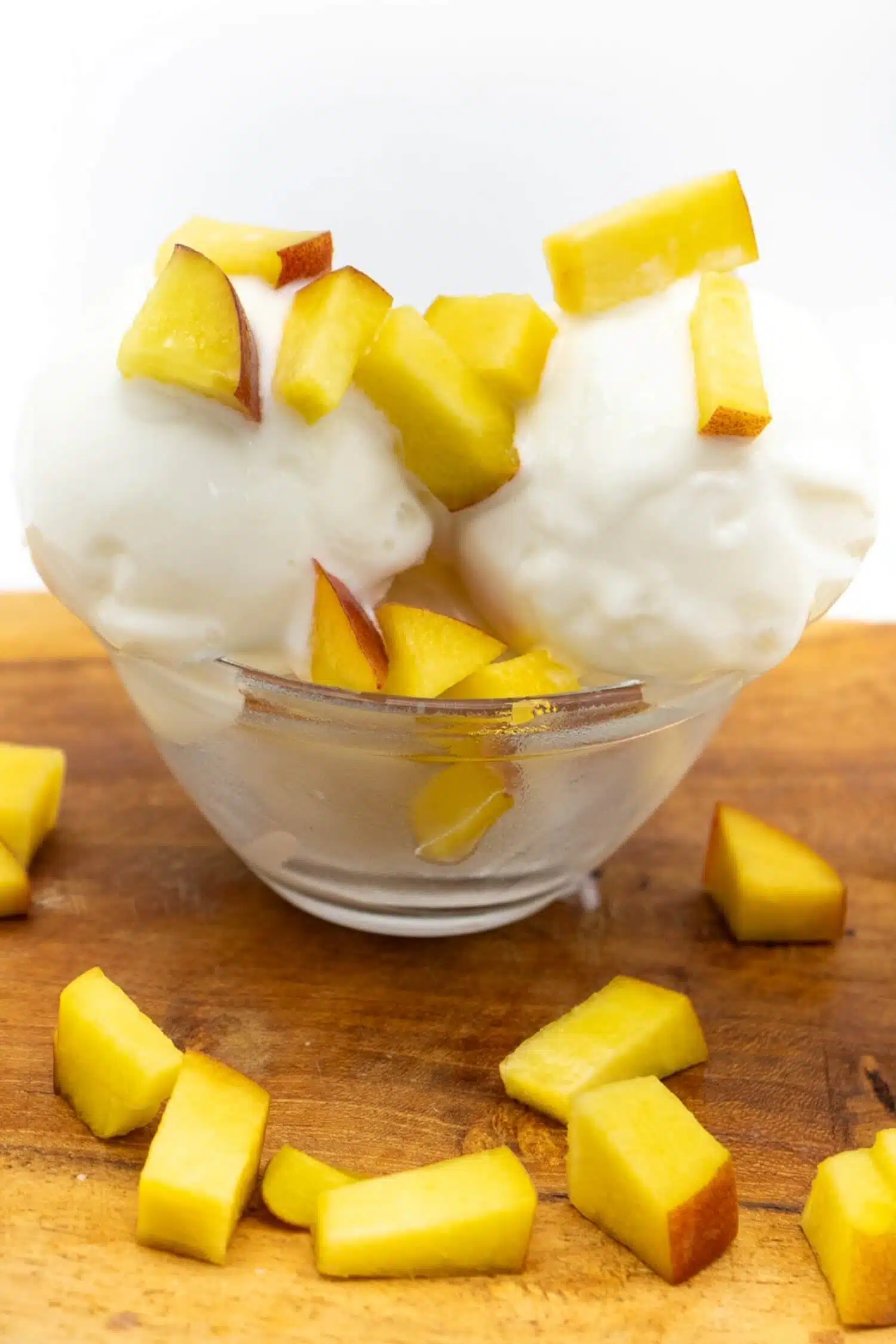 Zwei Kugeln kalorienarmes Joghurt Eis aus der Ninja Creami mit Pfirsichwürfeln in einer Glasschale
